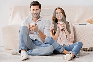 happy loving couple with cups of coffee resting on sofa