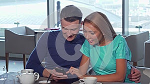 Happy loving couple embracing, using smart phone at the cafe together