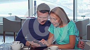 Happy loving couple embracing, using smart phone at the cafe together