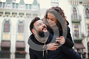 Happy loving couple hipster smiling and hugging each other outdoors having fun. The girl is on the back of a young guy