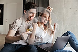 Happy loving couple in home using laptop computer holding credit card
