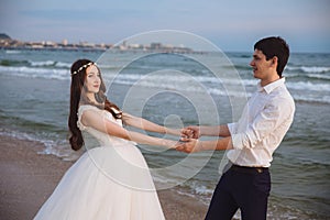 Happy loving couple newlyweds hold each others hands on ocean beach. Beautiful bride and groom at wedding day outdoors