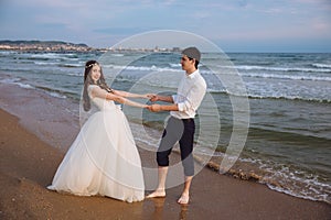 Happy loving couple newlyweds hold each others hands on ocean beach. Beautiful bride and groom at wedding day outdoors