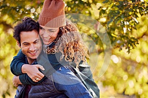 Happy Loving Couple Smiling As Man Give Woman Piggyback In Autumn Park