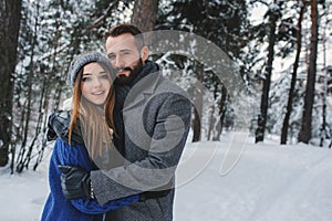 Happy loving couple walking in snowy winter forest, spending christmas vacation together. Outdoor seasonal activities