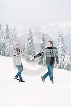 Happy loving couple walking in snowy winter forest, spending christmas vacation together. Outdoor seasonal activities. Lifestyle c