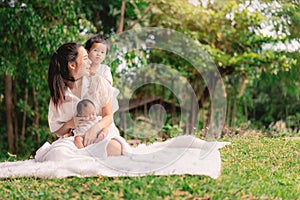 Happy loving family. Asian young beautiful mother and her children, new born baby girl and a boy sitting on green grass to playing