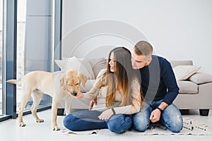 Happy Loving Family Concept. Portrait of beautiful couple with dog sitting on the floor in modern apartment