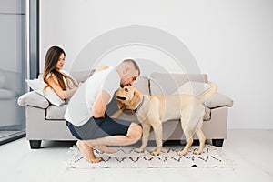 Happy Loving Family Concept. Portrait of beautiful couple with dog sitting on the floor in modern apartment