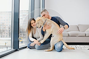 Happy Loving Family Concept. Portrait of beautiful couple with dog sitting on the floor in modern apartment