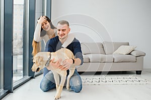 Happy Loving Family Concept. Portrait of beautiful couple with dog sitting on the floor in modern apartment