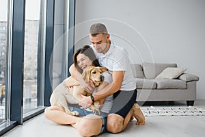 Happy Loving Family Concept. Portrait of beautiful couple with dog sitting on the floor in modern apartment