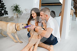 Happy Loving Family Concept. Portrait of beautiful couple with dog sitting on the floor in modern apartment