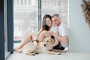 Happy Loving Family Concept. Portrait of beautiful couple with dog sitting on the floor in modern apartment