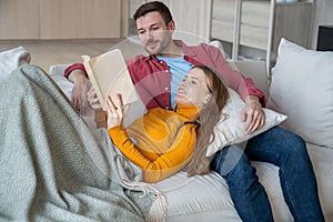 Happy loving family couple staying at home, relaxing, reading interesting novel, discussing on couch