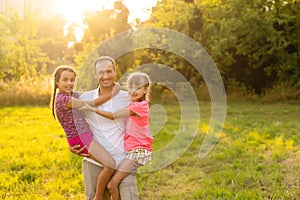 Happy loving family, dad playing with two little cute daughters outdoors at sunset, family relationship and friendship