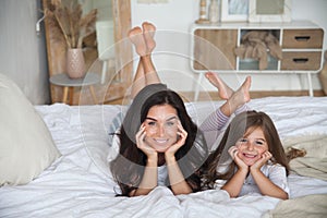 Happy loving family lying relaxing and enjoying in bedroom together. Mother and her cute preschool daughter child girl in pajamas