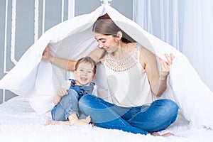 A happy, loving family. Mom and baby son play at home on the bed under the blanket