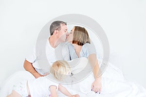 Happy and loving family morning concept. Kissing parents in sleepwear and back view daughter on the bed. Family spending free time