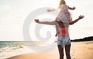 Happy loving family mother and daughter having fun on the beach at sunset - Mum piggyback with her kid next sea during summer