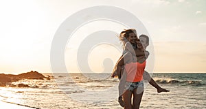 Happy loving family mother and daughter having fun on the beach at sunset - Mum piggyback with her kid next sea during vacations