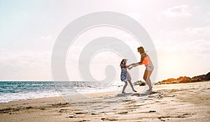 Happy loving family mother and daughter having fun on the beach at sunset - Mum playing with her kid next sea in holidays