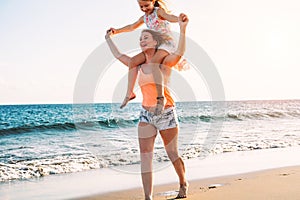 Happy loving family mother and daughter having fun on the beach in vacation - Mom carrying on shoulders her kid and running