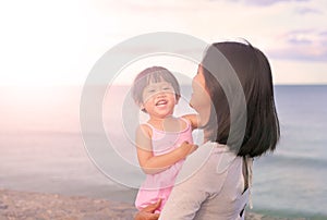 Happy loving family. Mother and her daughter child girl playing and hugging on sea background in the evening