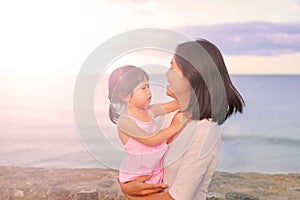 Happy loving family. Mother and her daughter child girl playing and hugging on sea background in the evenin