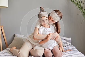 Happy loving family. Mother and her daughter child girl playing and hugging sitting on bed in bedroom woman kissing her cute child