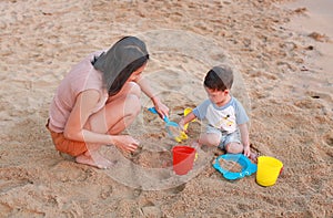 Happy loving family. Mother and her son playing sand at the beach with plastic toy