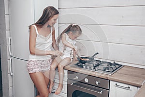 Happy loving family preparing cheesecakes for breakfast together. Beautiful young Mom and her cute child daughter girl cooking and