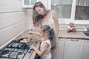 Happy loving family preparing cheesecakes for breakfast together. Beautiful young Mom and her cute child daughter girl cooking and