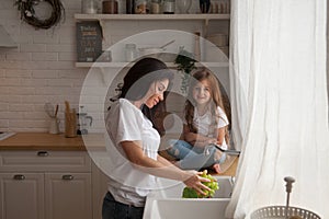 Happy loving family preparing food together. Smiling Mom and child daughter girl washing fruits and vegetables and