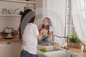 Happy loving family preparing food together. Smiling Mom and child daughter girl washing fruits and vegetables and having fun in