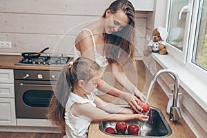 Happy loving family preparing food together. Smiling Mom and child daughter girl washing fruits and vegetables and having fun in