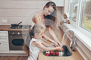 Happy loving family preparing food together. Smiling Mom and child daughter girl washing fruits and vegetables and having fun in