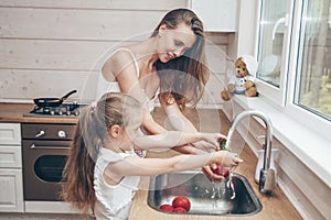Happy loving family preparing food together. Smiling Mom and child daughter girl washing fruits and vegetables and having fun in