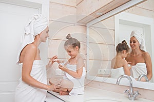 Happy loving family take care of the skin and apply moisturizer on face. Mother and her daughter child girl having fun in white