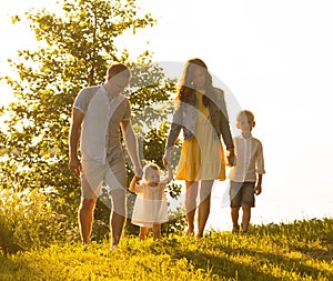 Happy loving family walking outdoor in the light of sunset. Father, mother, son and daughter.