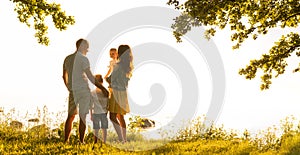 Happy loving family walking outdoor in the light of sunset. Father, mother, son and daughter.