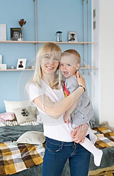 Happy loving family. Young blonde mother playing with her baby in the bedroom.