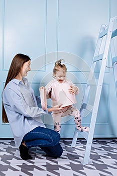 Happy loving family. young Mother in blue and her little daughter in pink clothes playing with pink gift box and blue ladder on