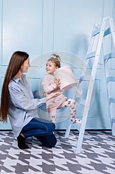 Happy loving family. young Mother in blue and her little daughter in pink clothes playing with pink gift box and blue ladder on