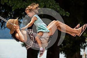 Happy loving family! Young mother and her child daughter swinging on the swings and laughing a summer evening outdoors, beautiful