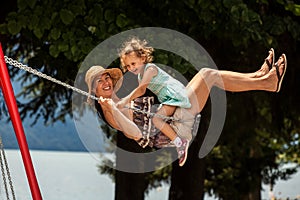 Happy loving family! Young mother and her child daughter swinging on the swings and laughing a summer evening outdoors, beautiful