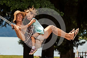 Happy loving family! Young mother and her child daughter swinging on the swings and laughing a summer evening outdoors, beautiful