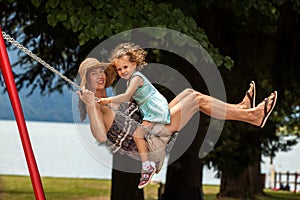 Happy loving family! Young mother and her child daughter swinging on the swings and laughing a summer evening outdoors, beautiful