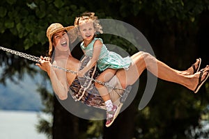 Happy loving family! Young mother and her child daughter swinging on the swings and laughing a summer evening outdoors, beautiful