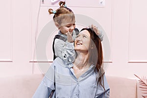 Happy loving family. young Mother and her little daughter playing and hugging on pink sofa and wall background. happy mother`s,